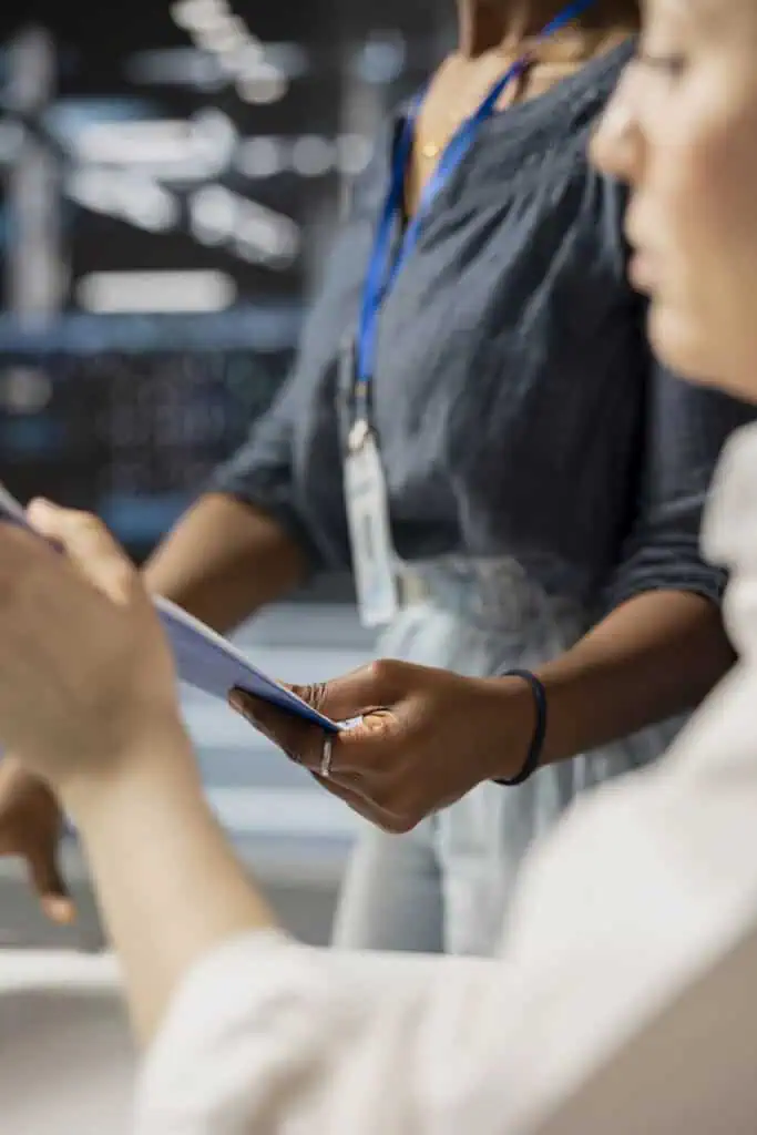 Two people looking at a document together in an office setting, both wearing ID badges. The focus is on their hands and the document, with blurred faces and background.