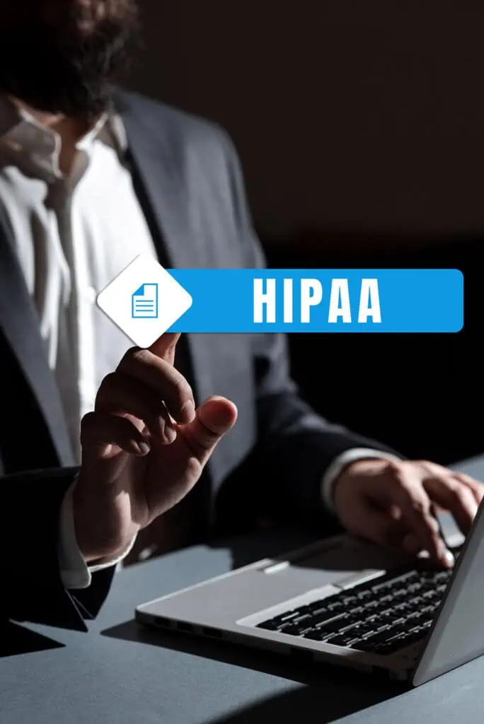 A person in a suit sits at a laptop, pointing at a floating digital button labeled HIPAA with a document icon, emphasizing data privacy and security.